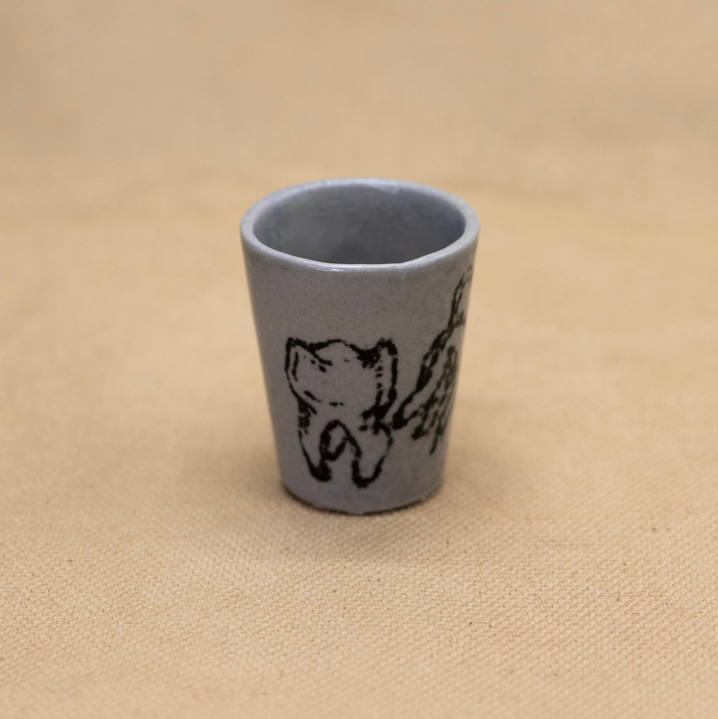 A ceramic shot glass with a custom hand drawn tooth decal