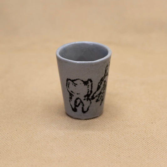 A ceramic shot glass with a custom hand drawn tooth decal